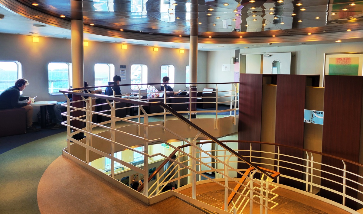 Interior of the Camellia Line ferry: staircase, lounge area with tables and window seats
